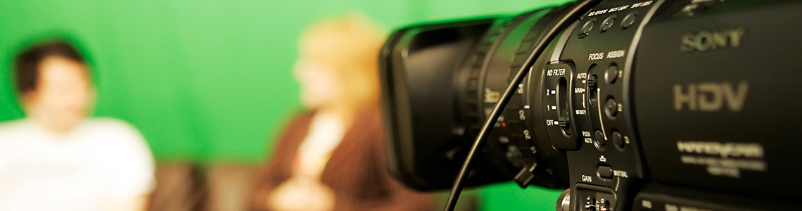 A professional camera pointed towards two people seated on a couch