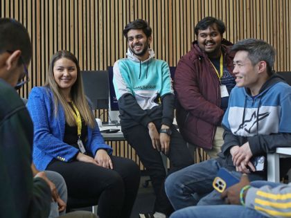 Image shows 5 students of various different backgrounds sitting around talking