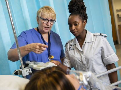 A nurse teaching a student nurse practicing on a dummy patient.