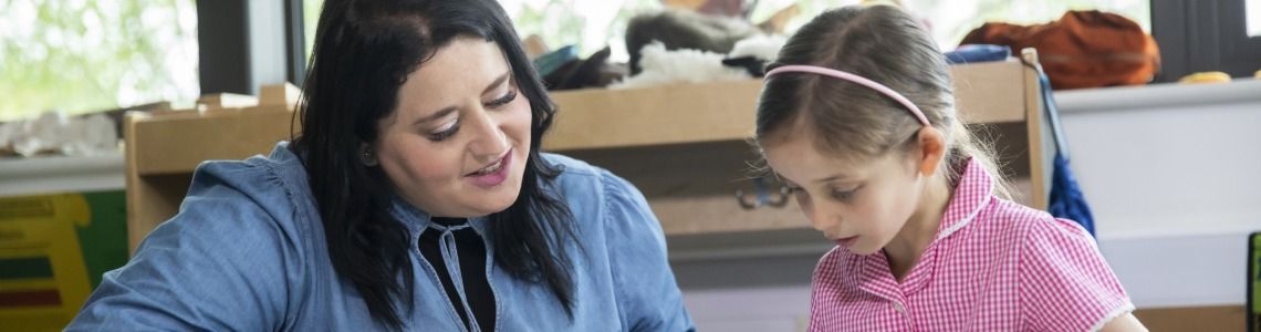 Female teacher interacting a young girl student in a classroom.